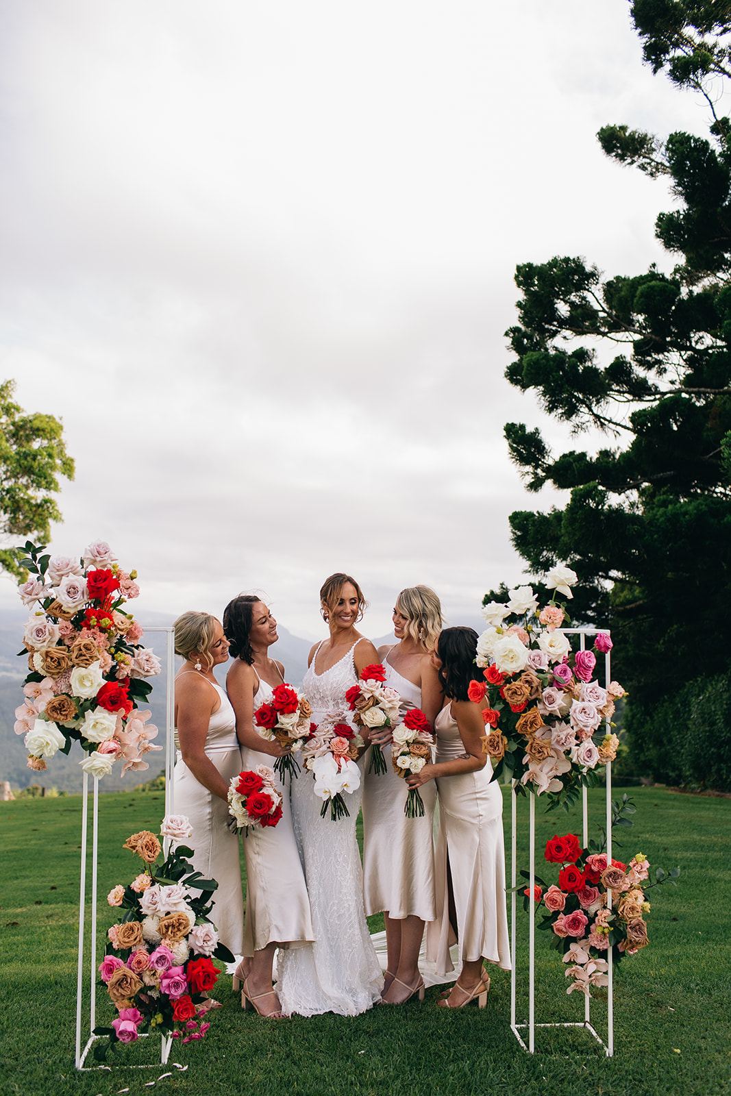 A bride with her bridesmaids between floral pillars on the lawn