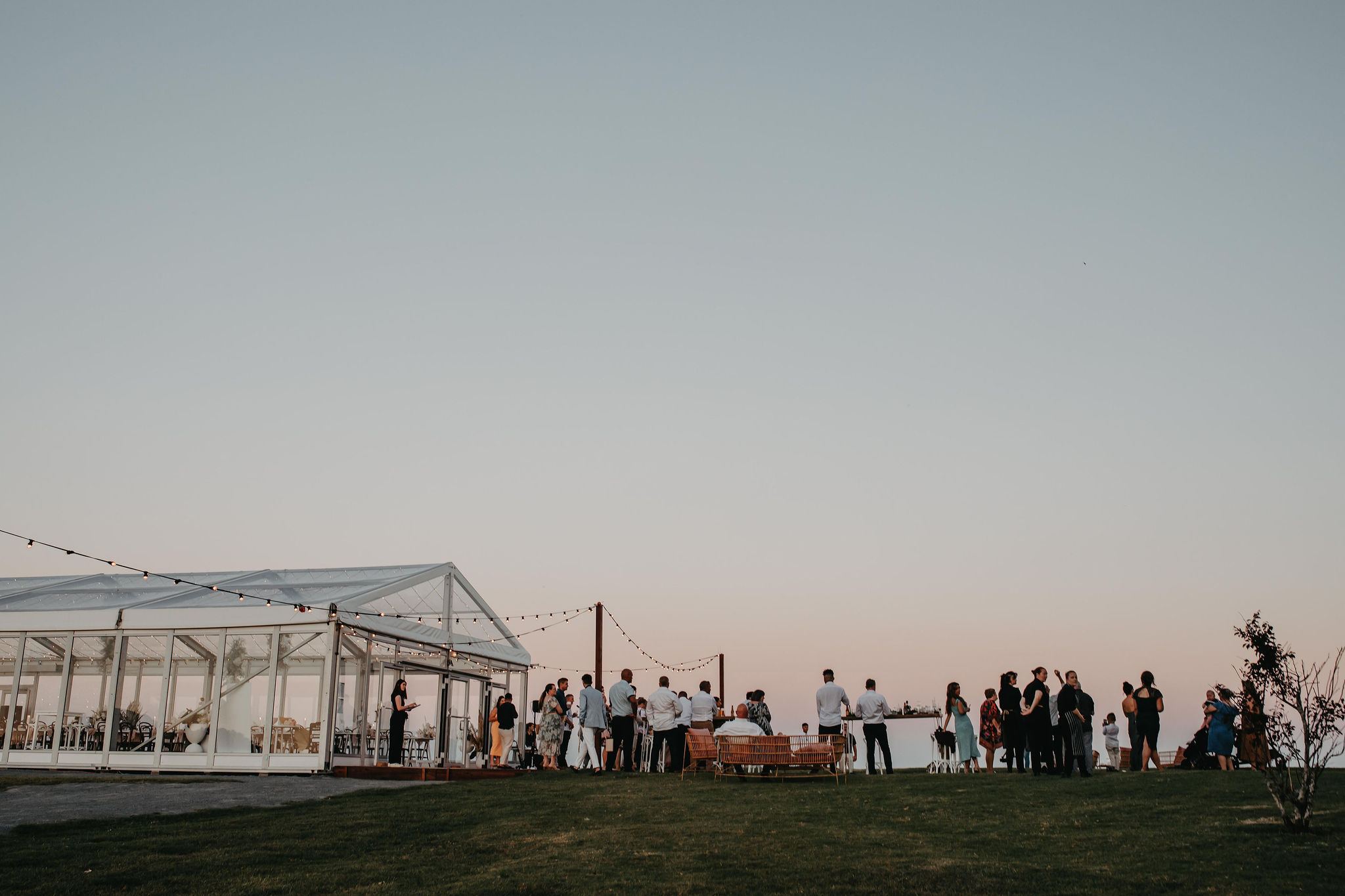 Guests with drinks outside the front of the marquee as the sun goes down