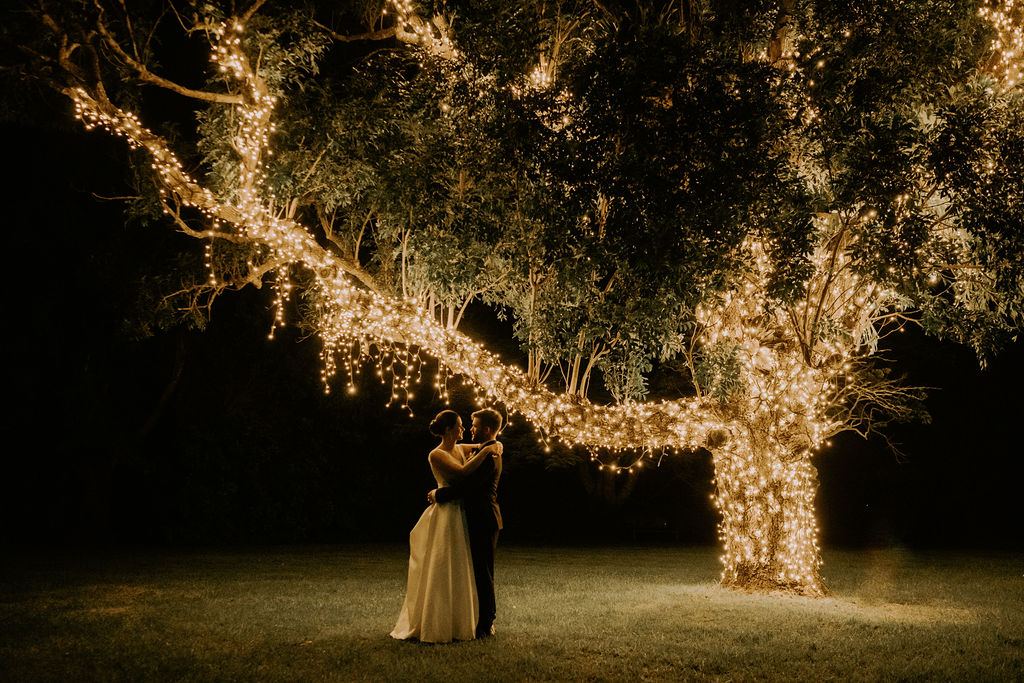 A couple beneath the fairy-light tree at night