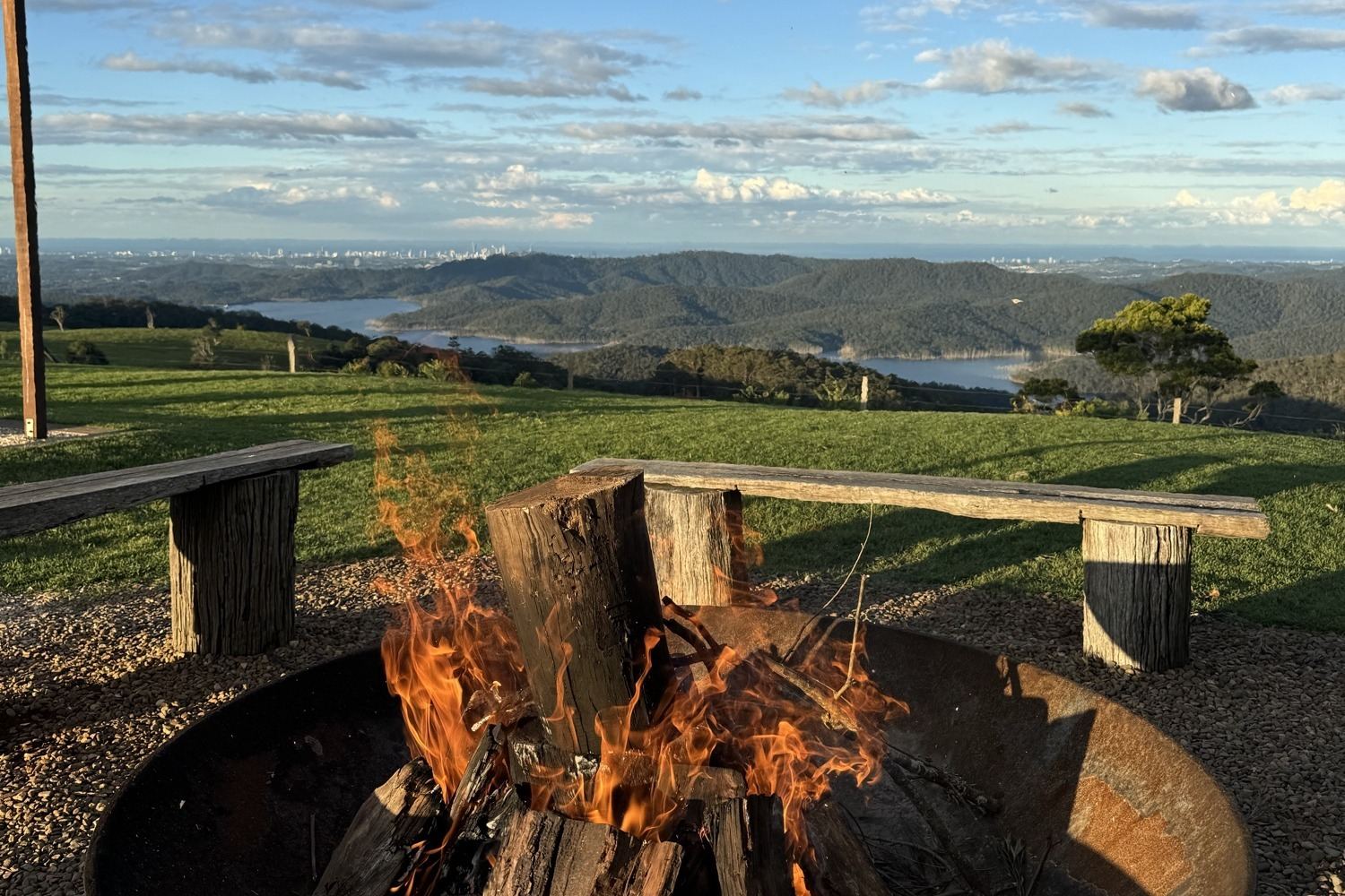 The Rosewood fire pit alight, timber benches around it and Hinze Dam below