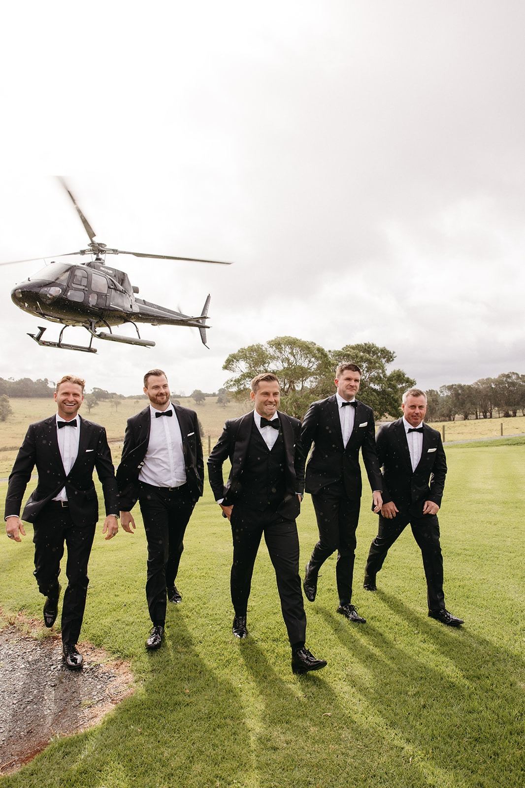 Groomsmen walking across the lawn as a helicopter lifts off behind them